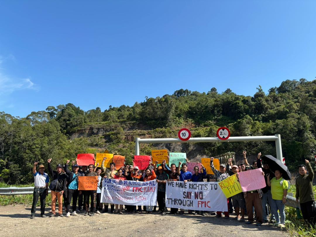 a group of community members hold protest signs against the tutoh dam project